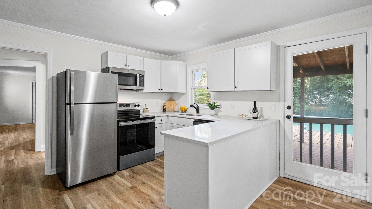 Bright white kitchen with a large island, stainless steel appliances, and a glass door opening to a covered deck.