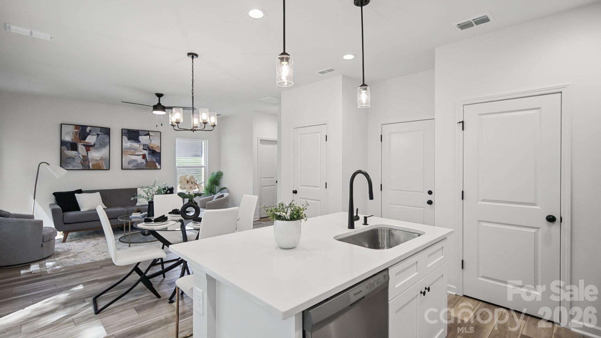 Open-plan kitchen with a large white island, black faucet, dining table, and gray living room sofa.