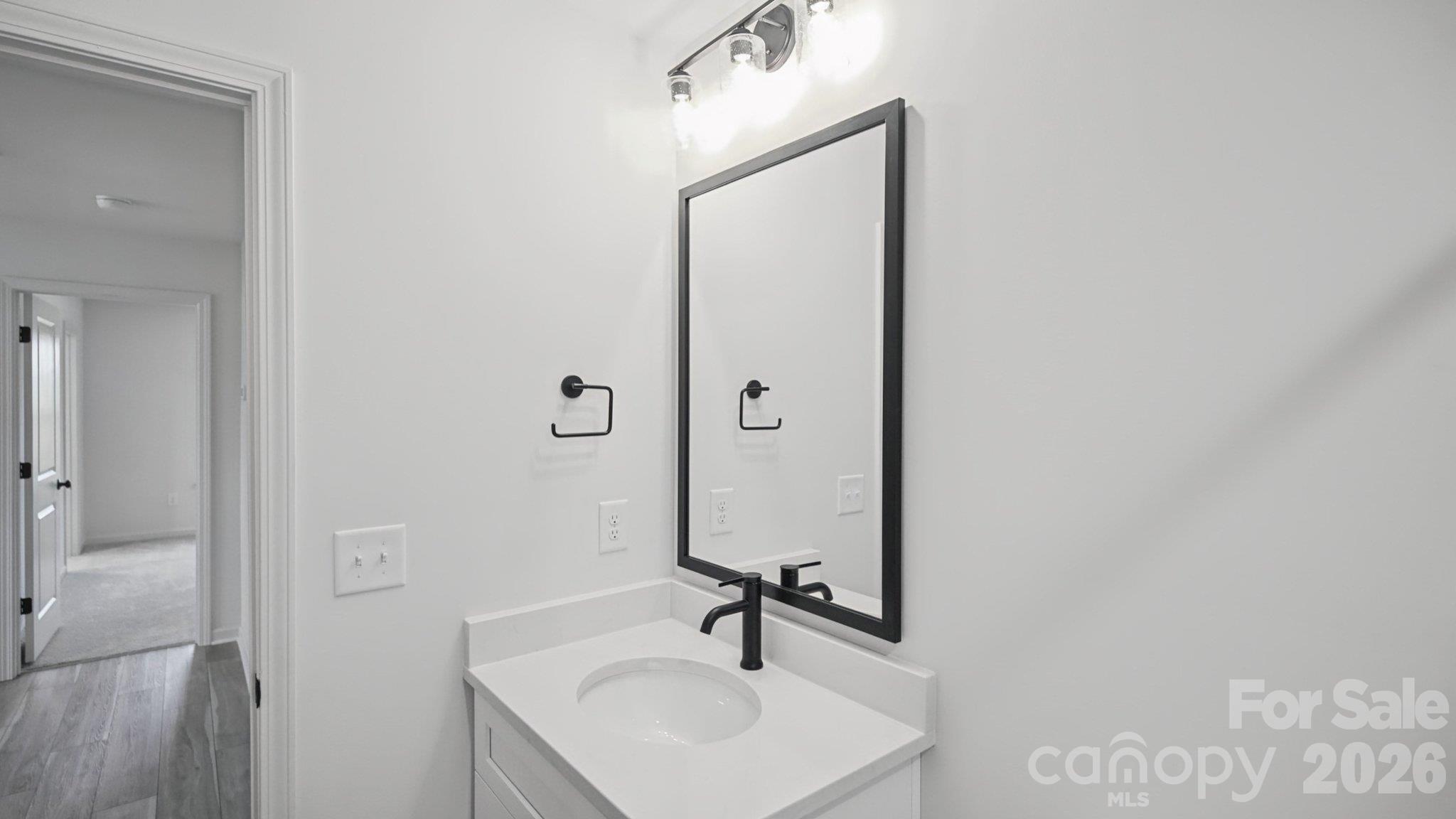 Bathroom vanity with an oval sink, matte black faucet, and large black-framed mirror.