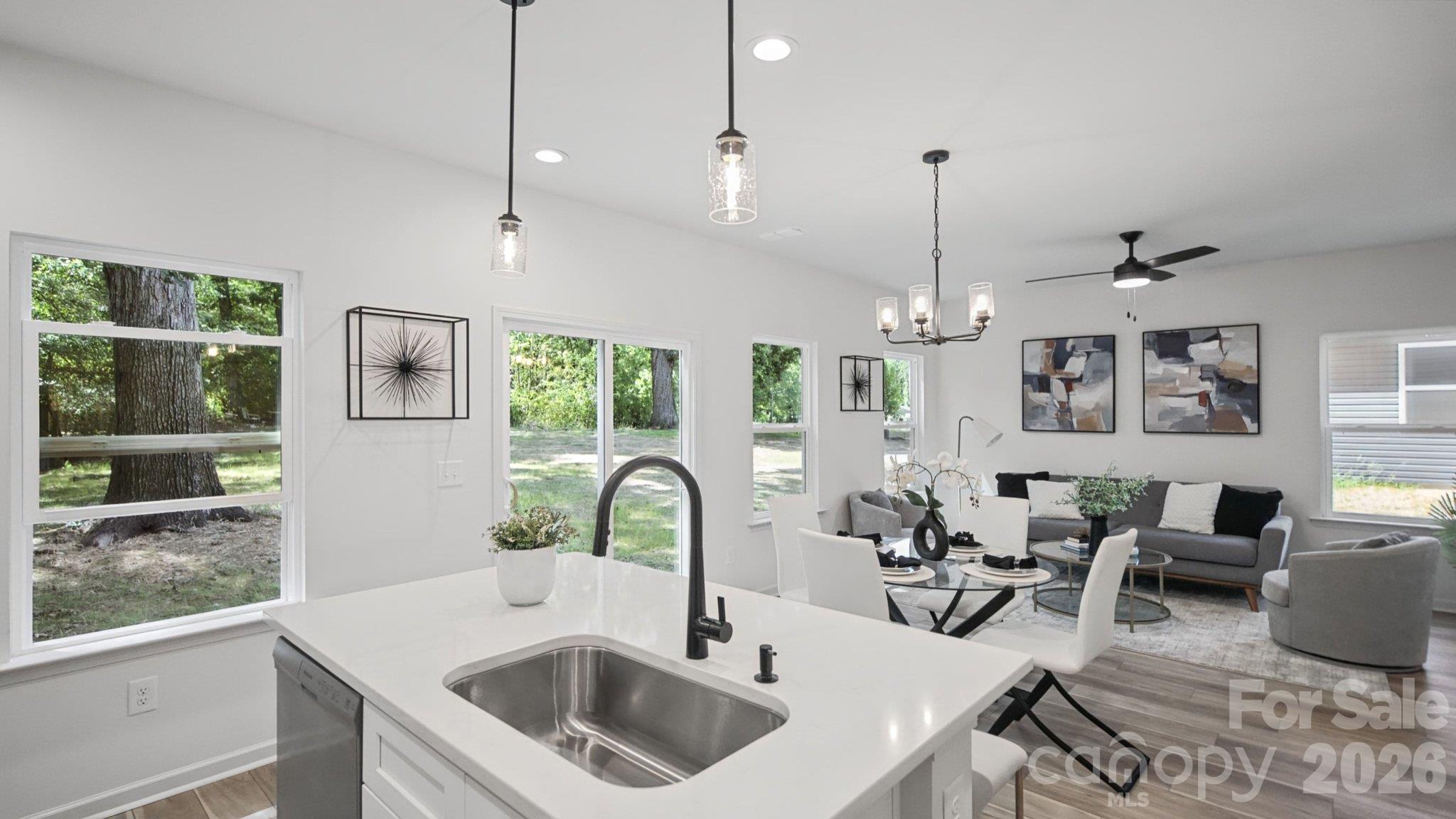 Open-plan kitchen and living room with a white island, black faucet, large windows, and gray seating.