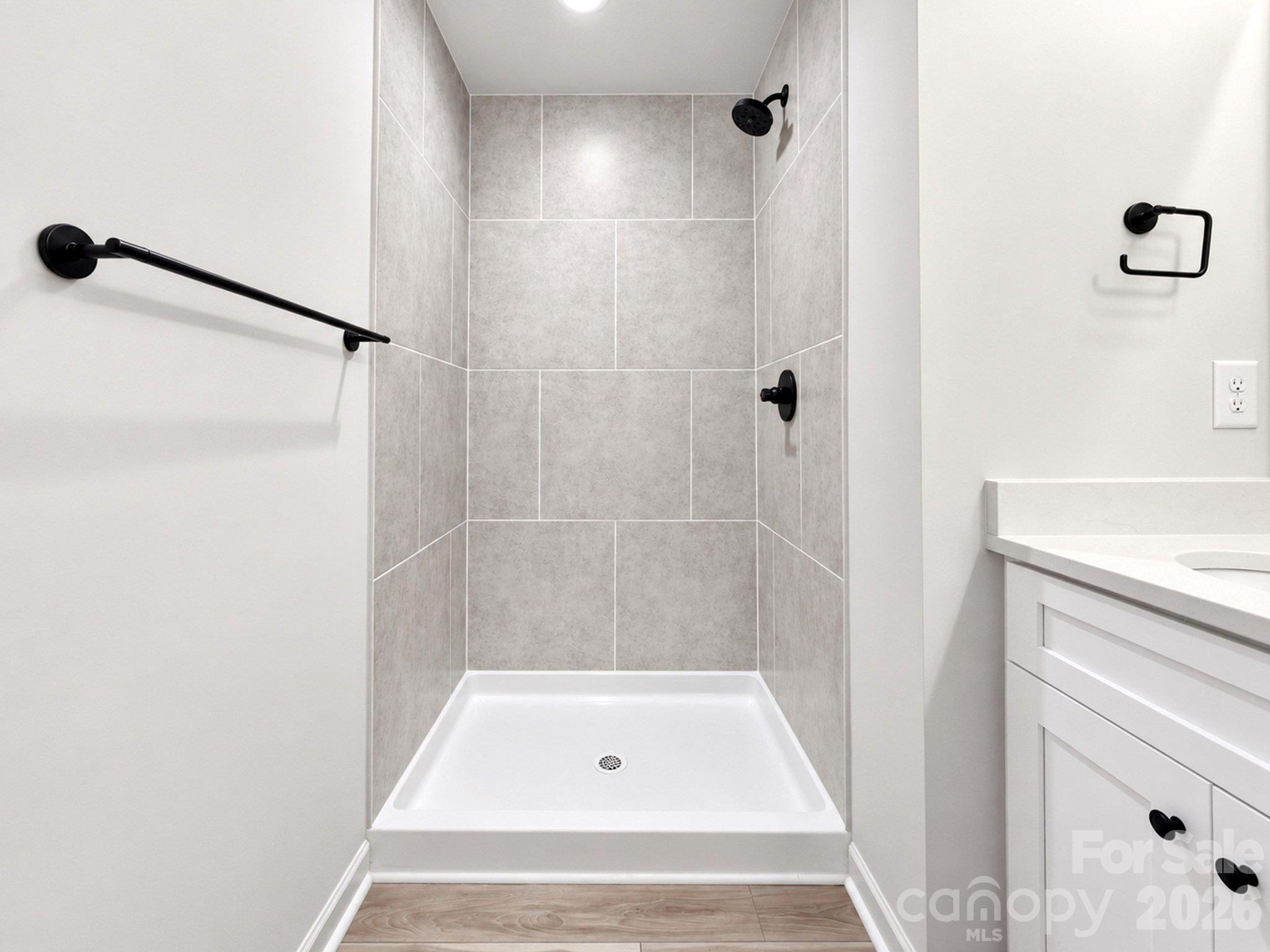 Bathroom walk-in shower with gray tile, black fixtures, and a white vanity.