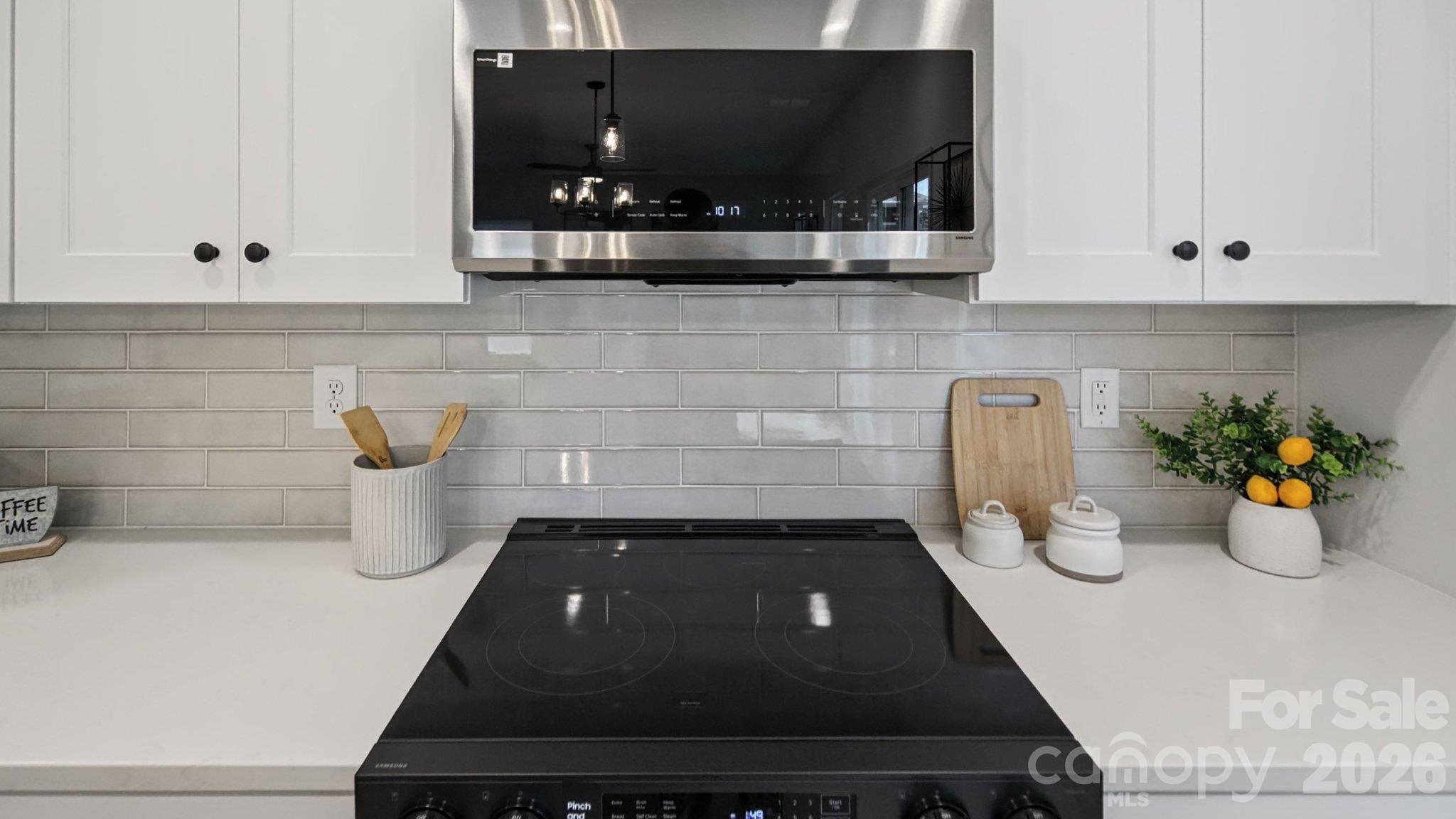 Kitchen cooktop beneath a stainless steel range hood, with white cabinets and gray subway tile backsplash.
