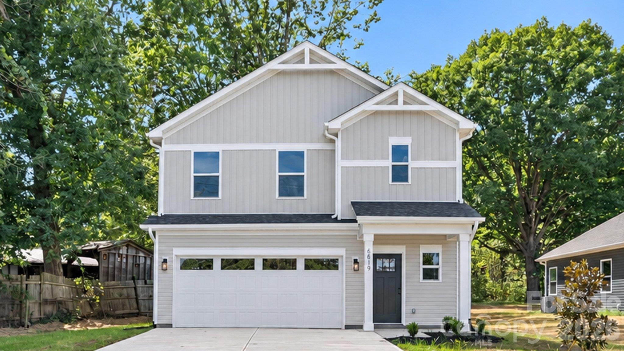 Two-story light gray house with white gables, a two-car garage, and mature trees.
