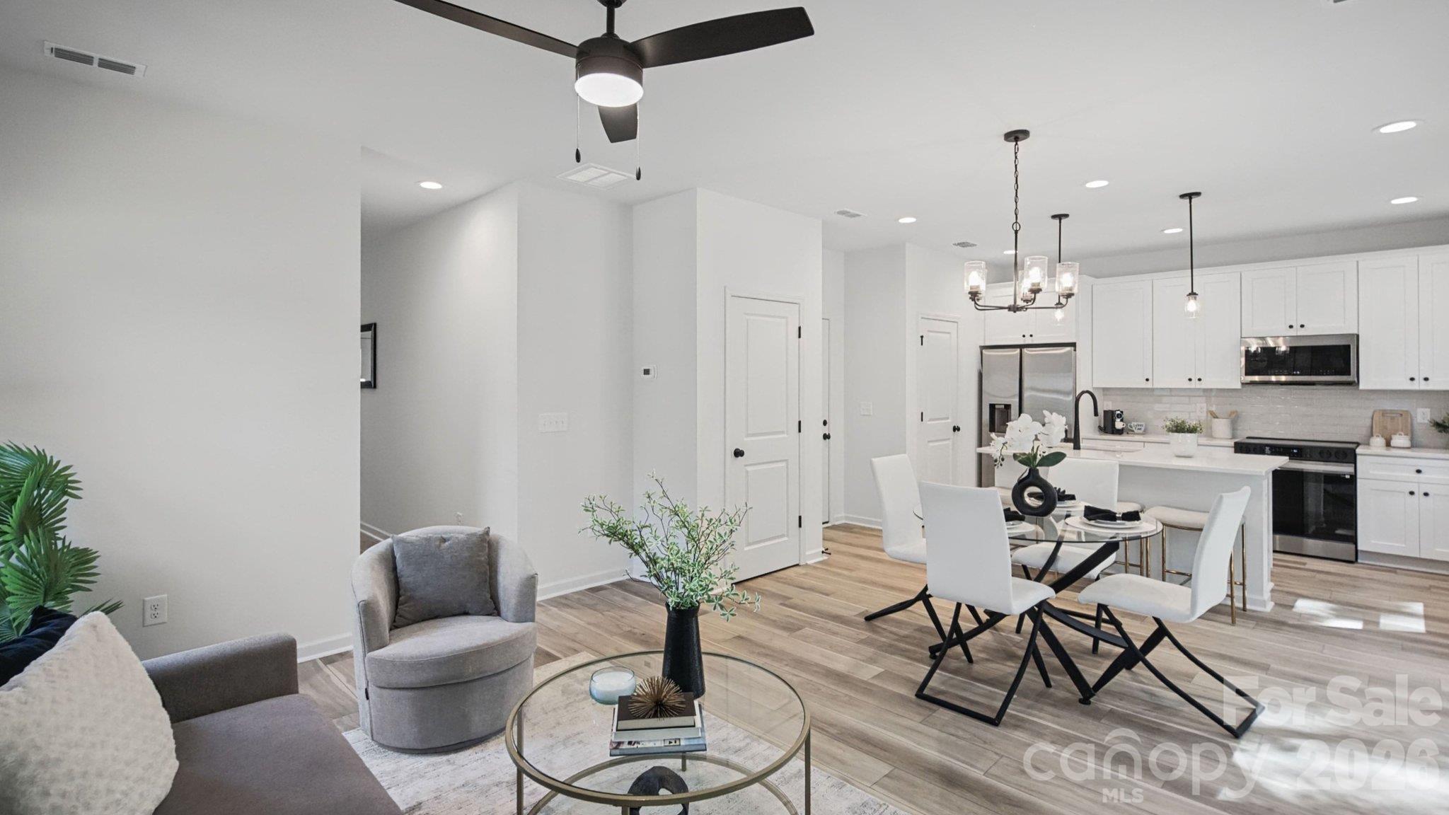 Open-plan living and dining room with a bright white kitchen, large island, and light wood floors.
