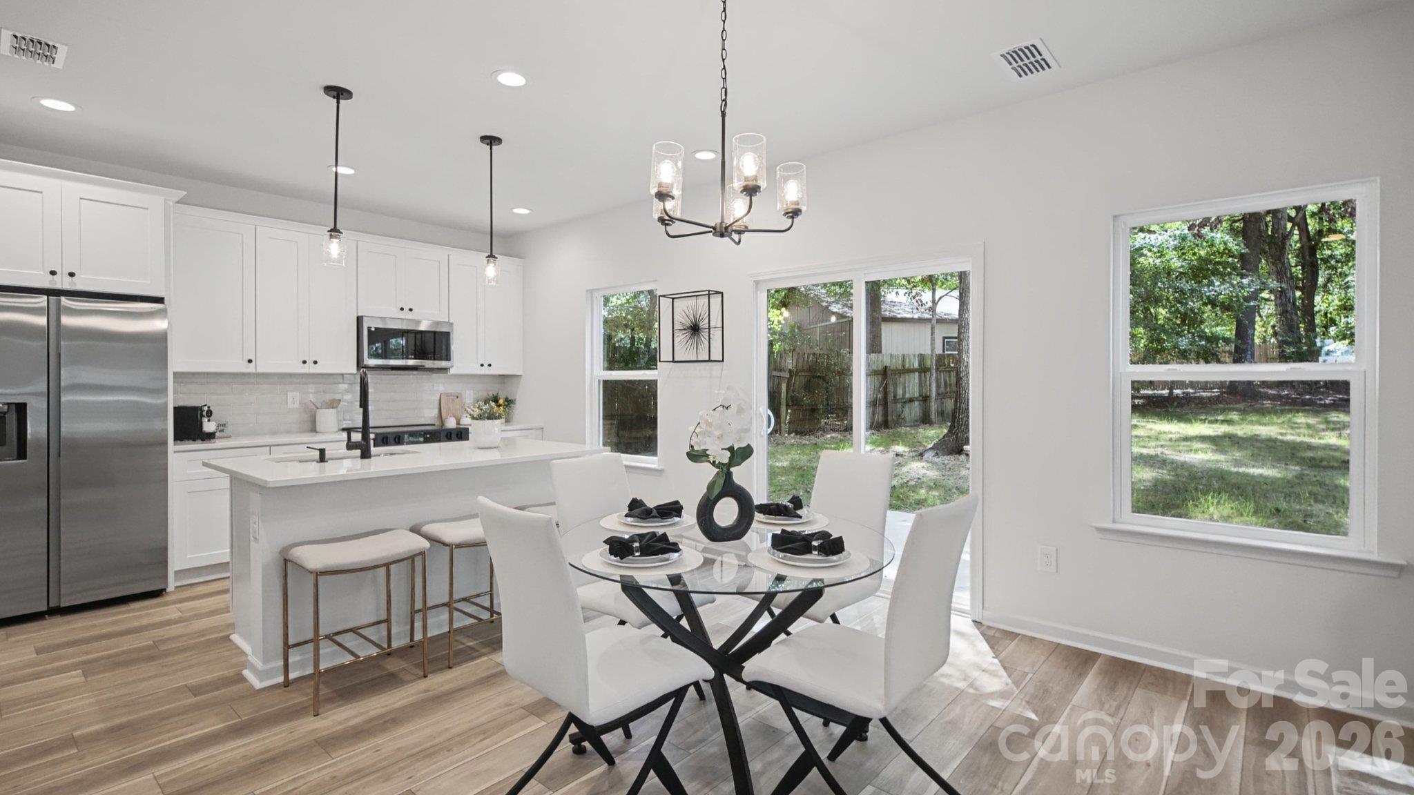 Bright kitchen and dining area with a white island, glass table, and windows overlooking the backyard.