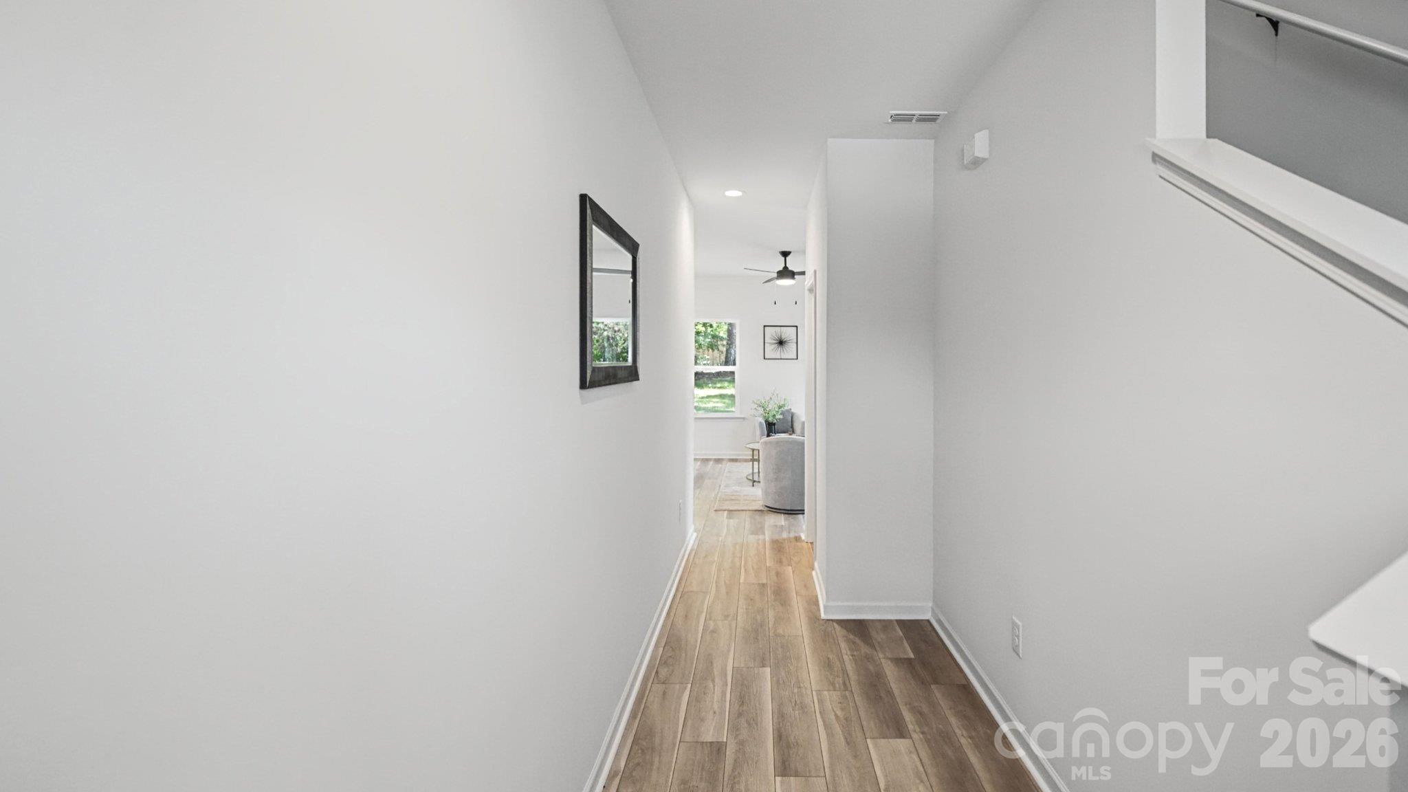 Bright hallway with wood-look flooring, a dark-framed mirror, and a staircase railing.