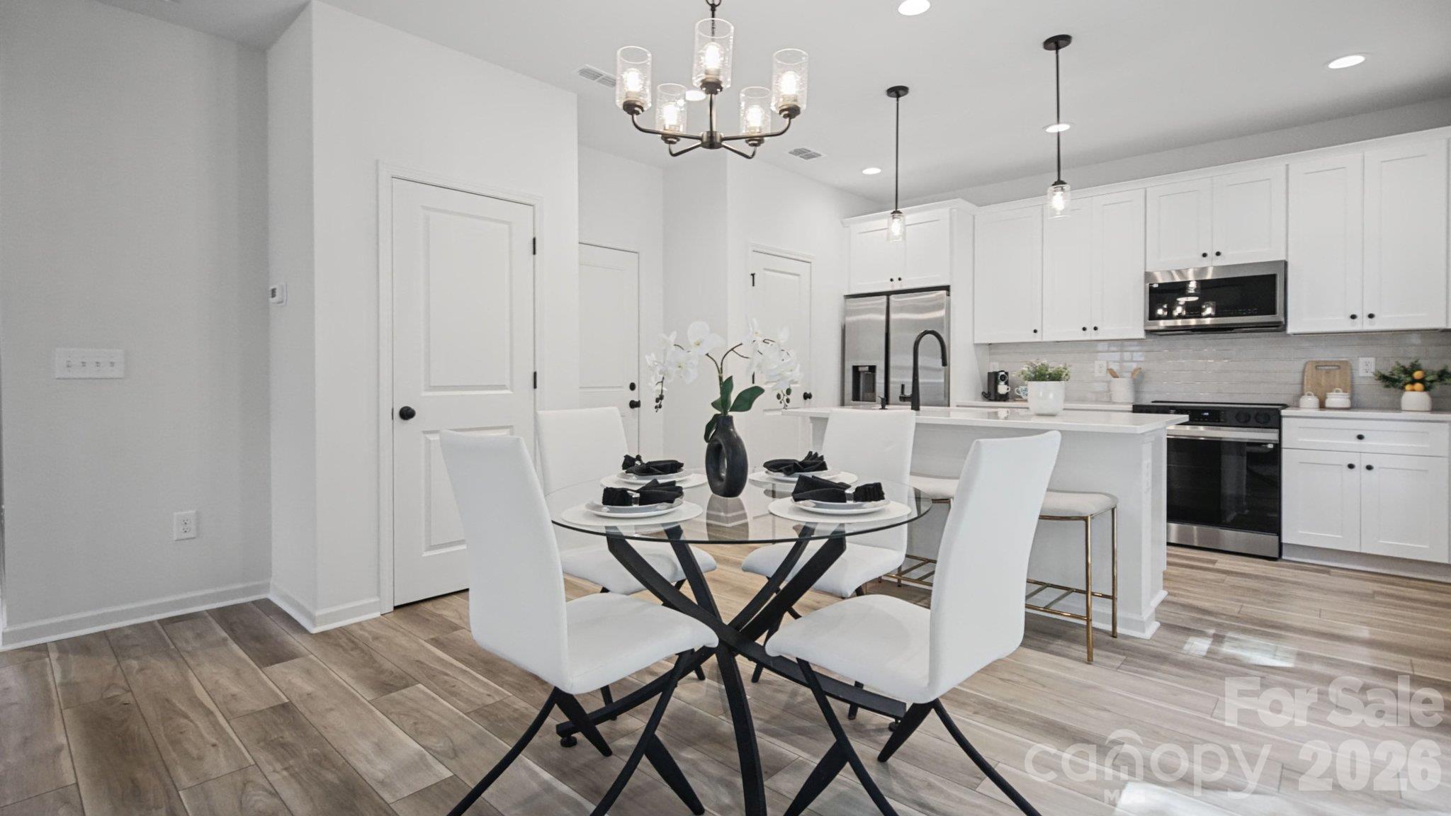Staged kitchen and dining area with white cabinetry, stainless steel appliances, and a glass dining table.