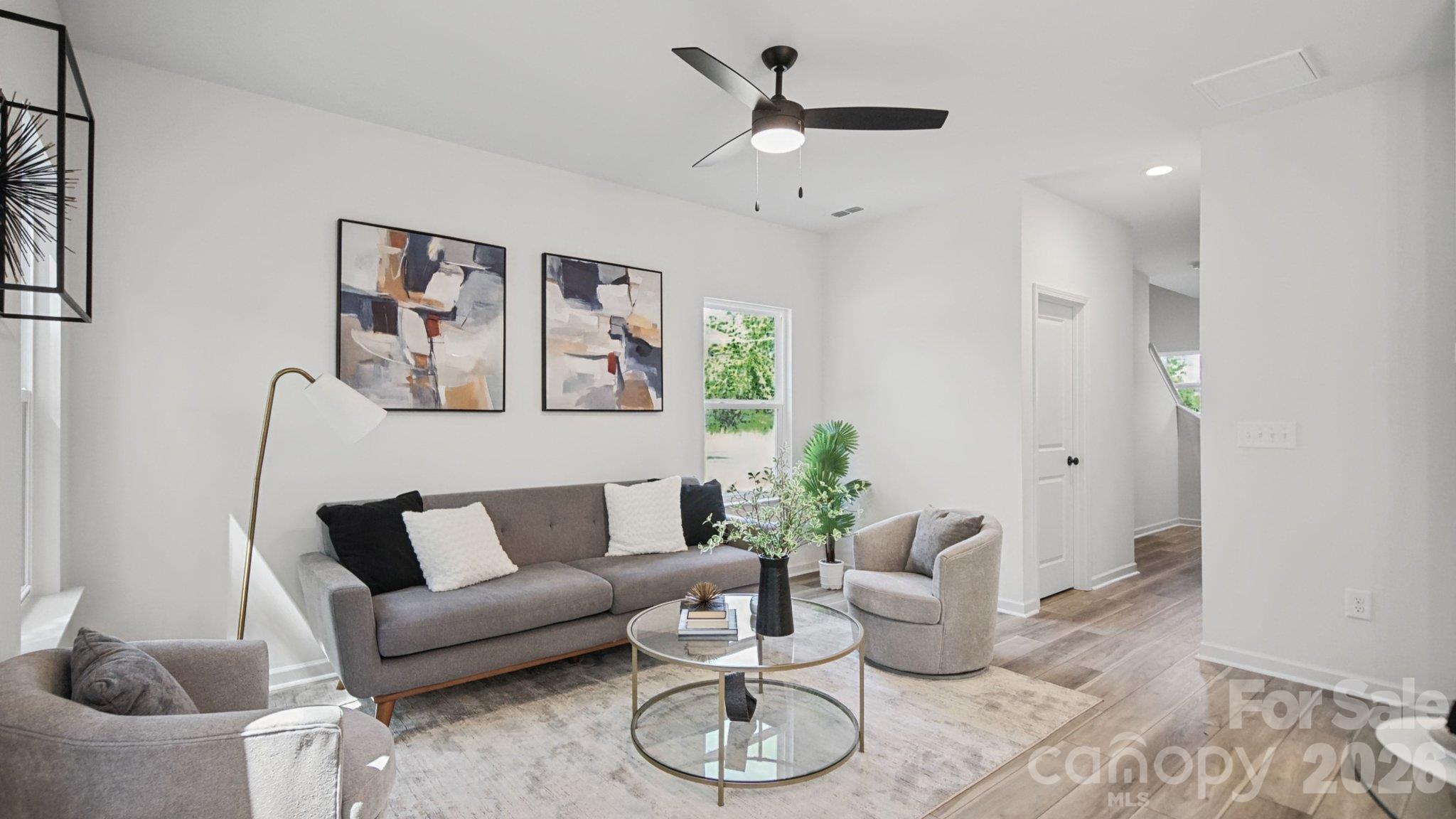 Furnished living room with a gray sofa, glass coffee table, abstract art, and ceiling fan.
