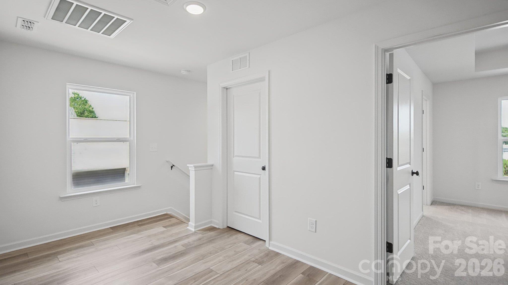 Empty room with light plank flooring, a window, and doors leading to a carpeted room.