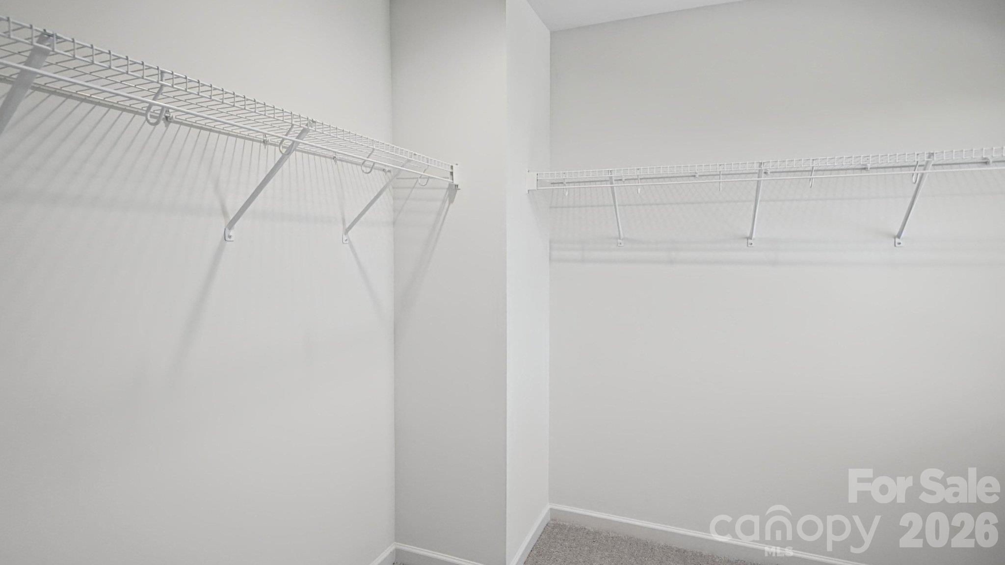 Empty walk-in closet with wire shelving on two walls and gray carpet.