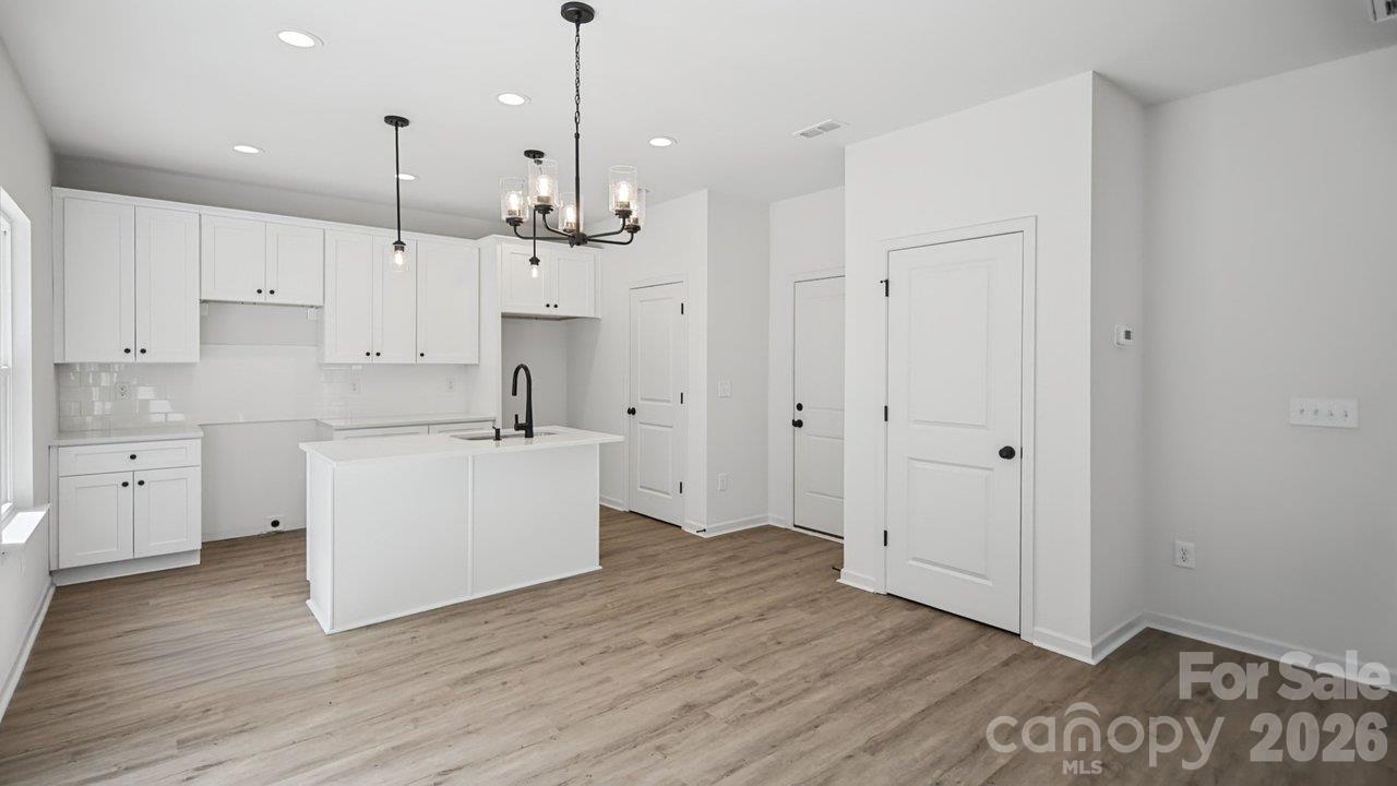 Empty kitchen with white cabinets, a central island, black faucet, and wood-look flooring.