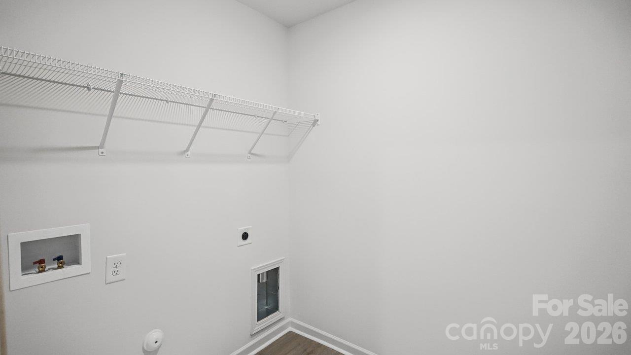 Empty laundry room with a long wire shelf, washer hookups, and a small window.