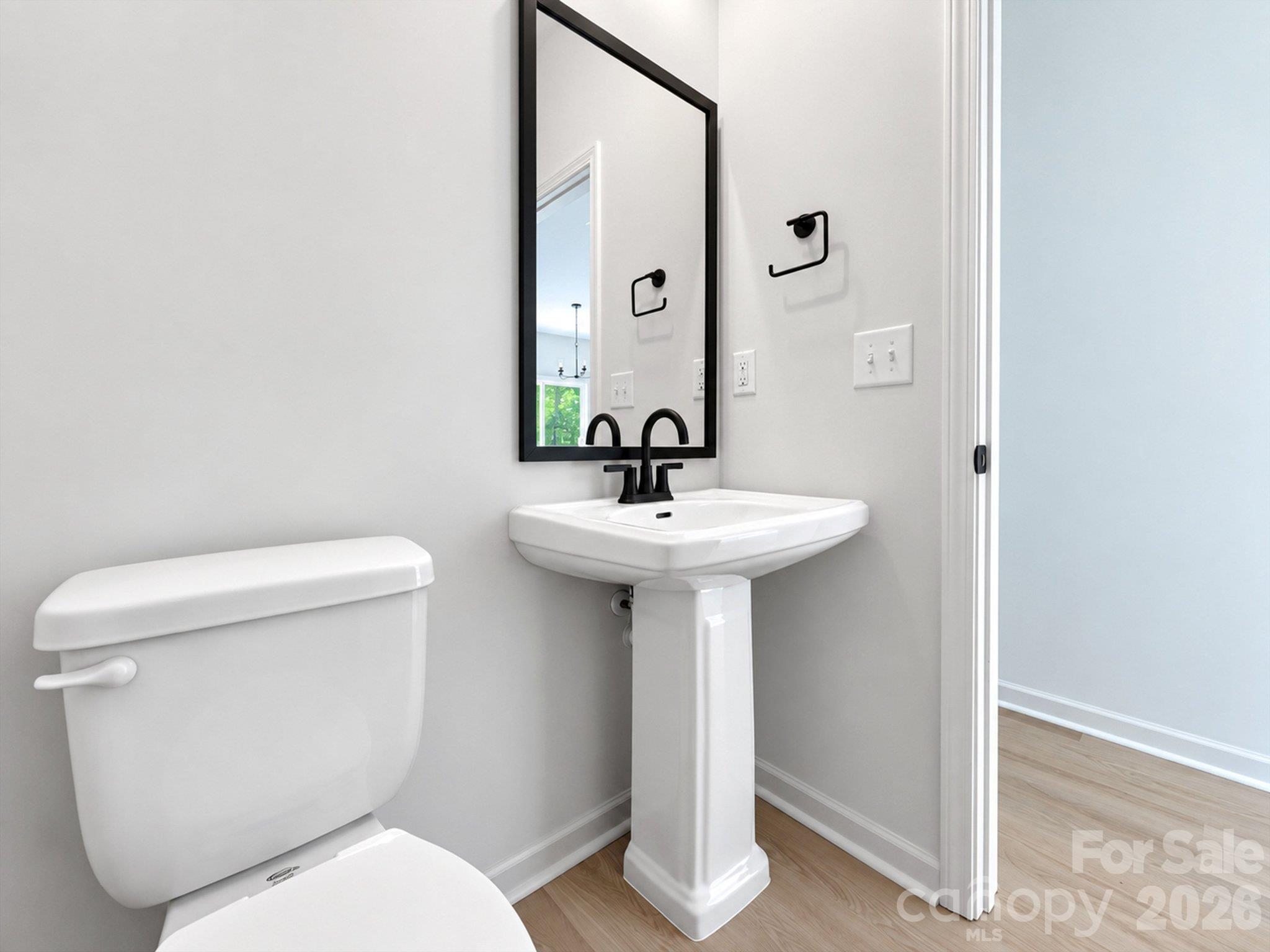 Bathroom with a white pedestal sink, toilet, black fixtures, and a large framed mirror.