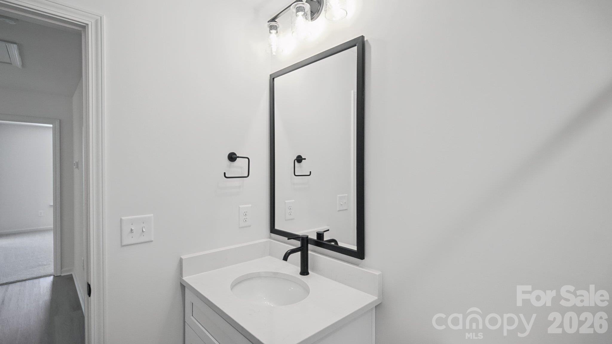 Bathroom vanity with an oval sink, matte black faucet, and large black-framed mirror.