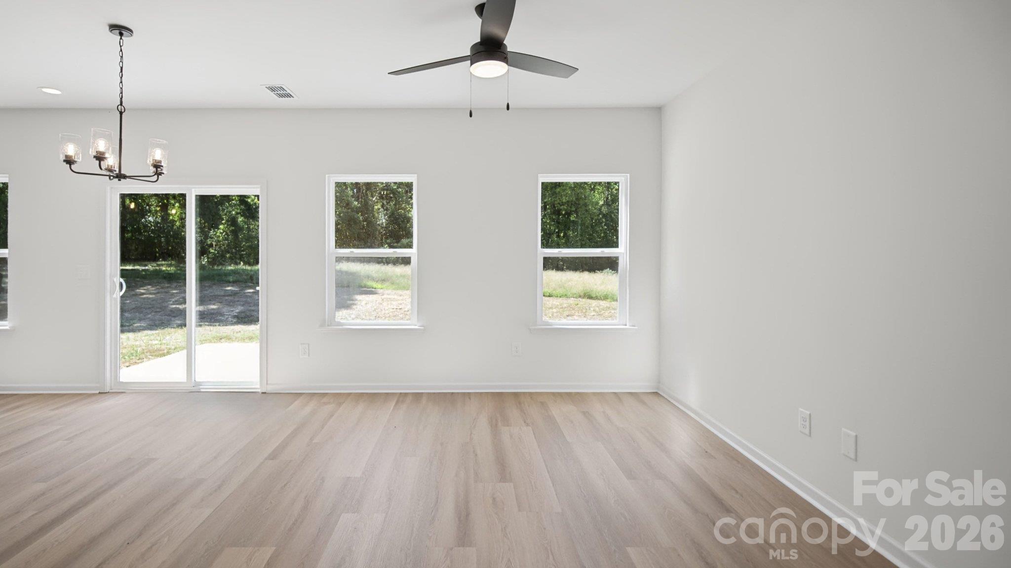 Empty living area with pale wood flooring, a ceiling fan, and sliding glass doors opening toward the yard.