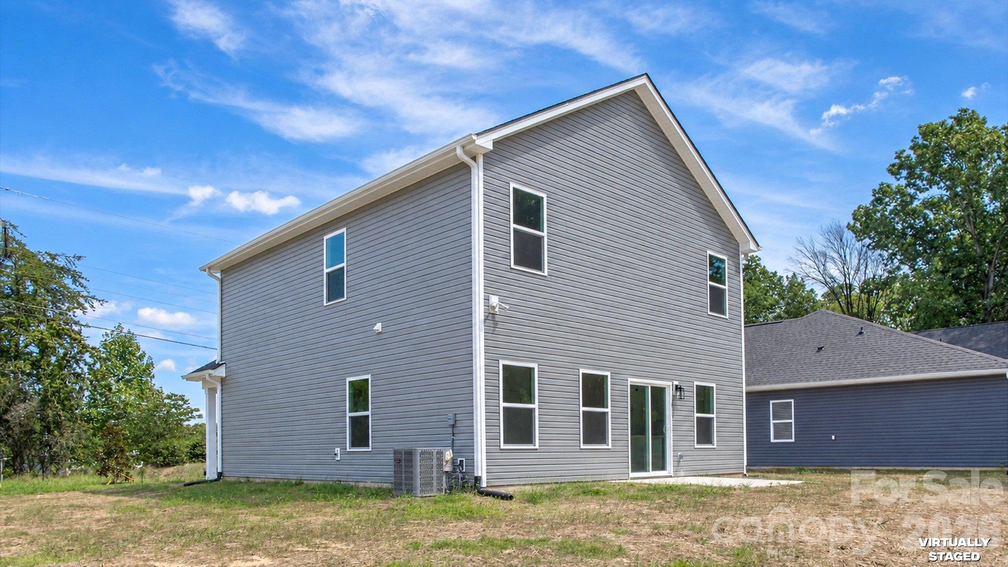Rear of a two-story gray-sided home with white trim, multiple windows, and a glass patio door.