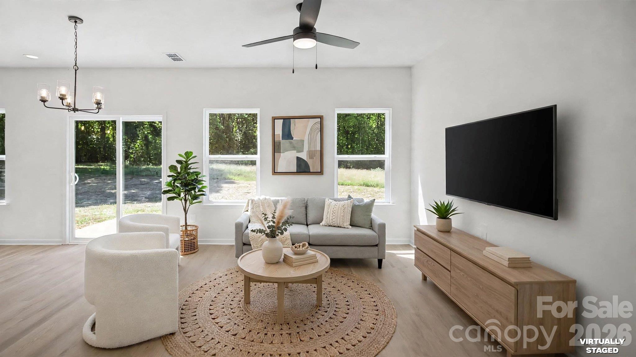 Virtually staged living room with a gray sofa, woven rug, wall-mounted TV, and sliding glass door.