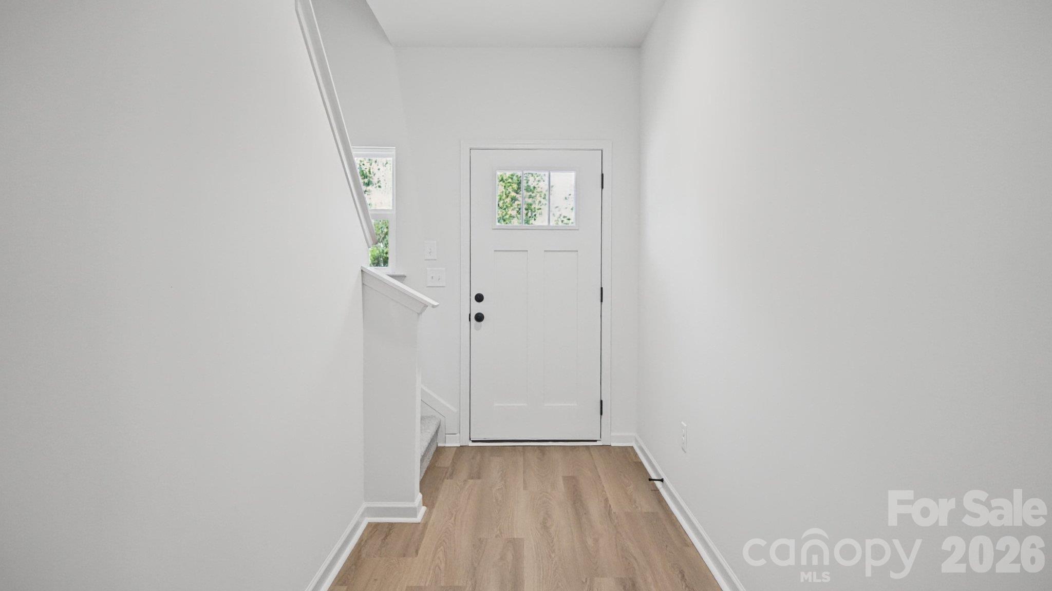 Vacant entryway with a white windowed front door, light wood flooring, and stairs to the left.
