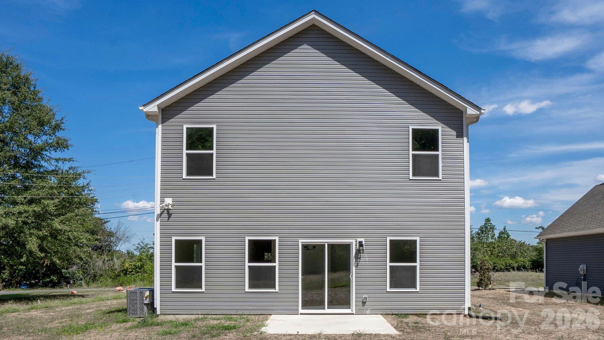 Two-story gray-sided house with a sliding glass patio door and a mostly bare yard.