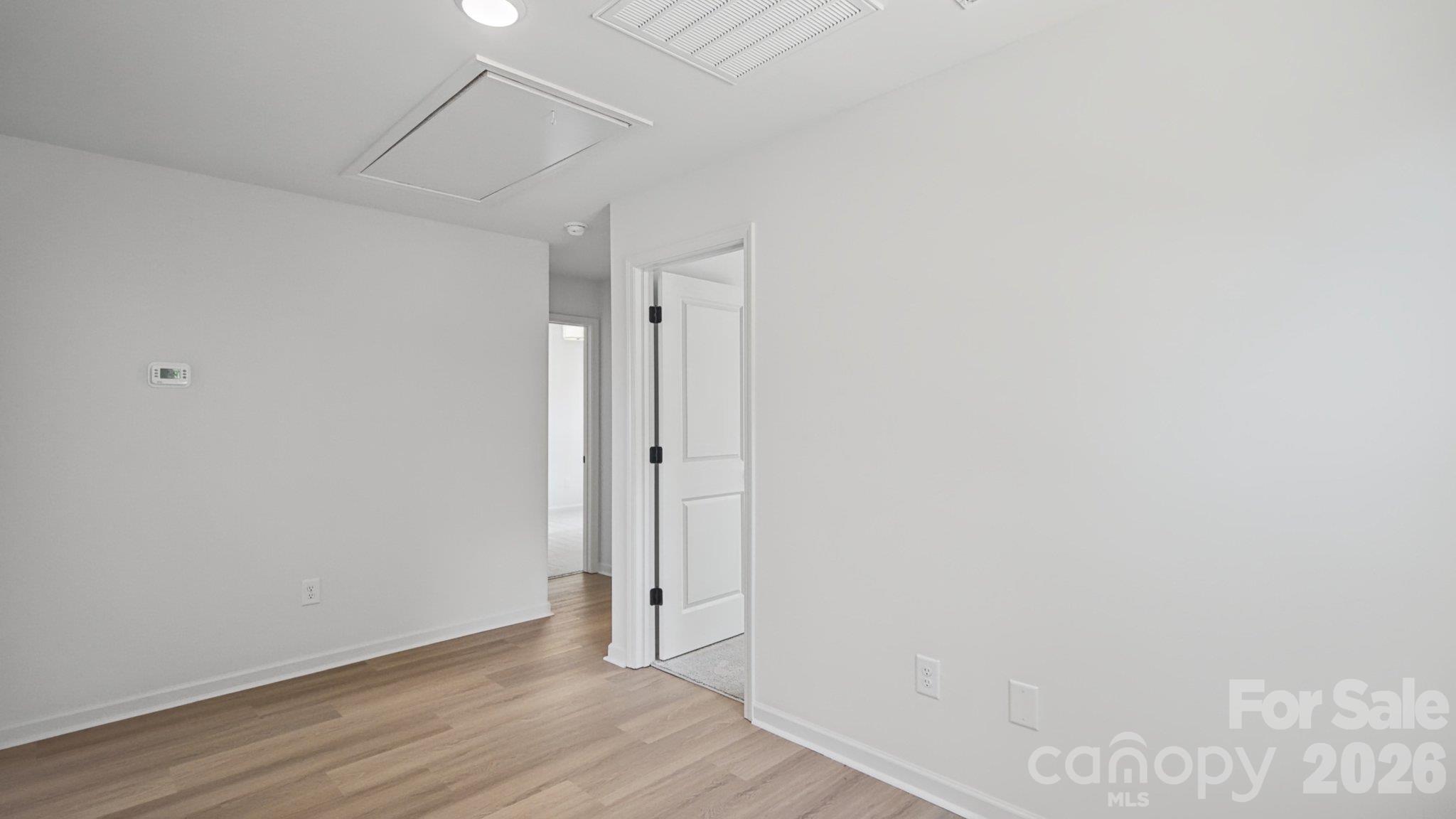 Empty room with light wood flooring, white walls, and an open doorway to adjoining rooms.