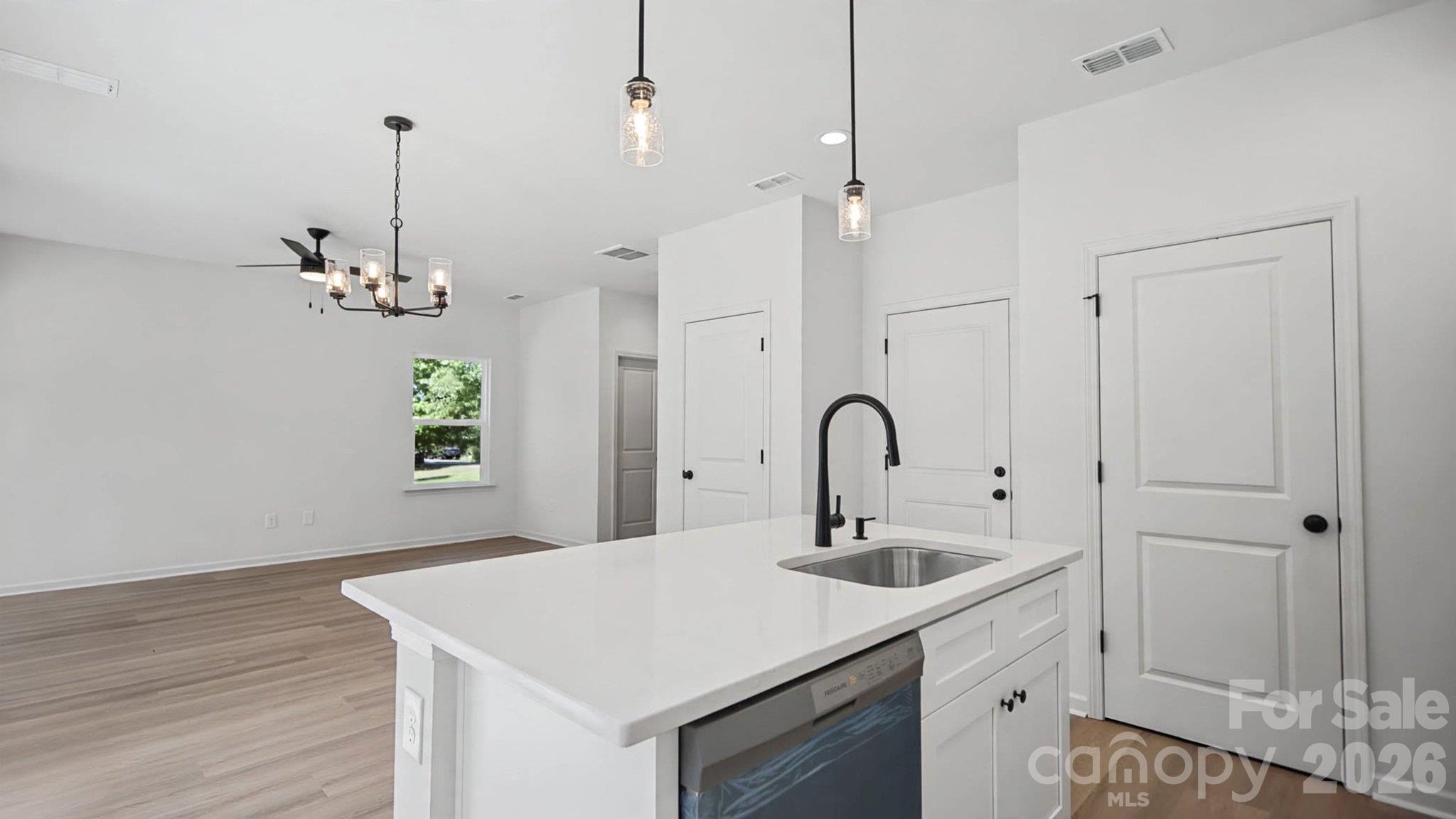 Vacant kitchen with a white island, black faucet, pendant lights, and open living area.