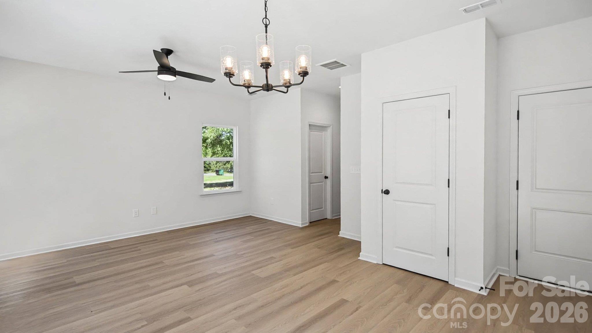 Vacant room with light wood floors, a window, ceiling fan, and chandelier.