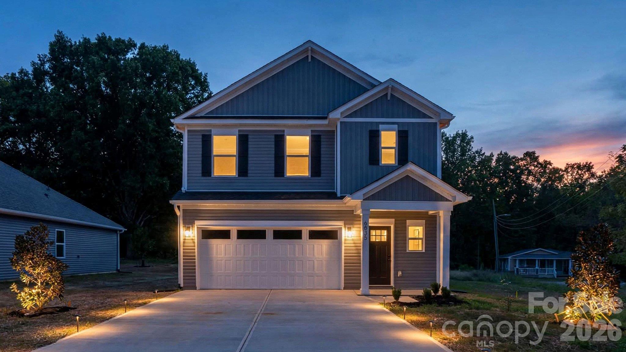 Two-story gray house with a double garage and warmly lit windows at dusk.