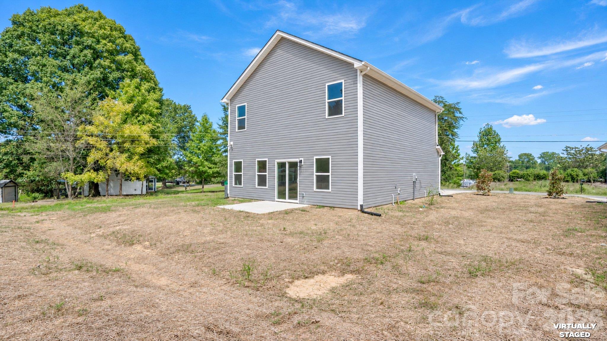 Gray two-story house with sliding glass doors and a broad, mostly bare yard.