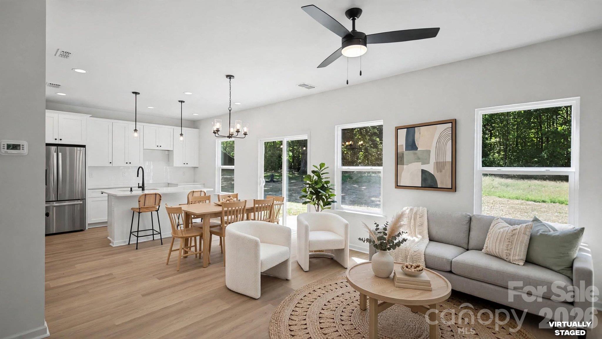 Virtually staged open-plan living room and kitchen with a gray sofa, dining table, and large windows.