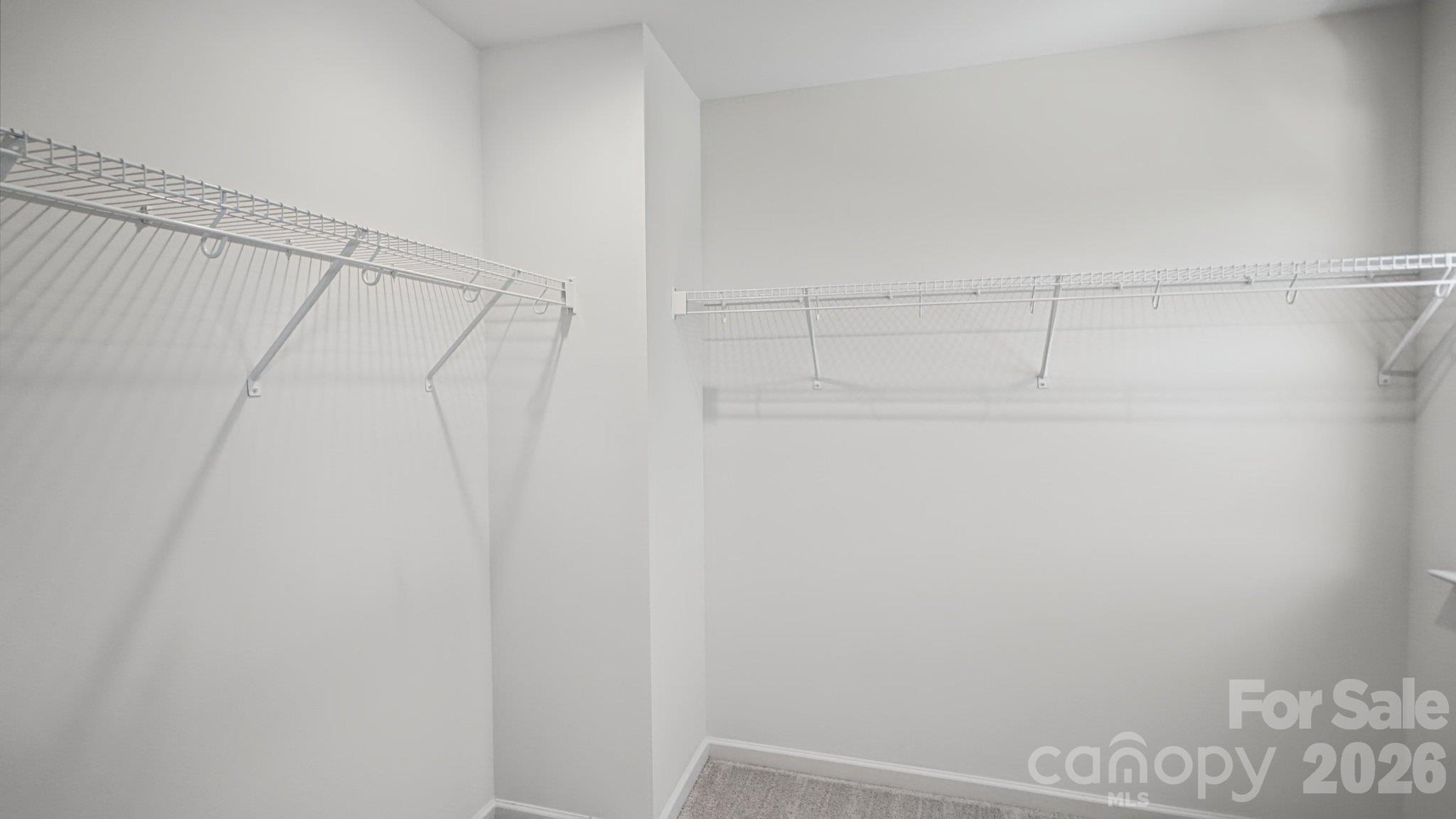 Empty walk-in closet with white wire shelving along two walls and carpeted flooring.