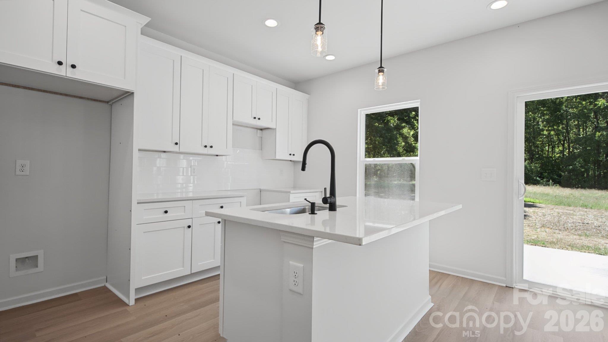 Bright white kitchen with shaker cabinets, a large island, and black faucet overlooking a wooded yard.