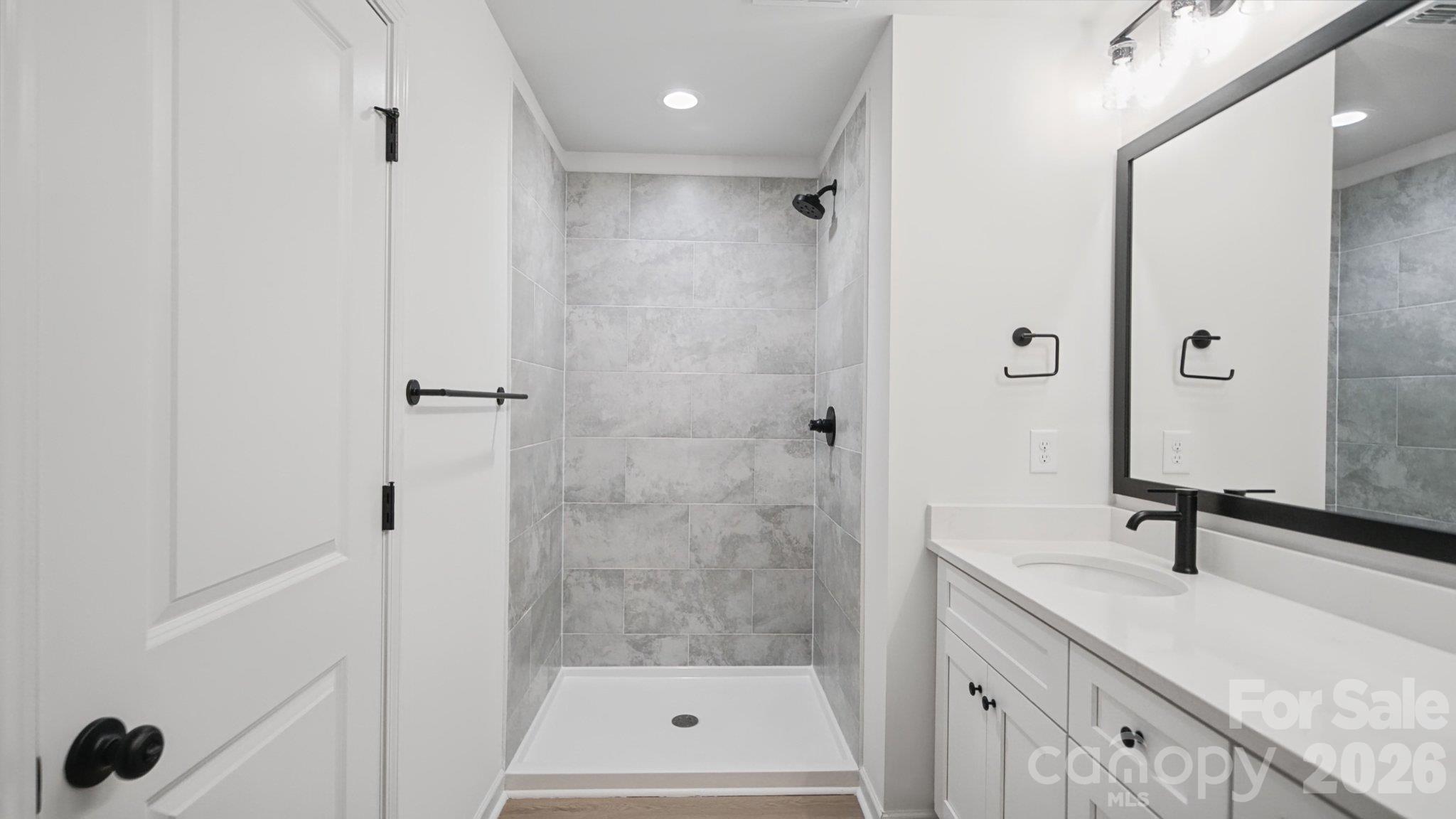 Bathroom with a gray-tiled walk-in shower, white vanity, black fixtures, and large framed mirror.