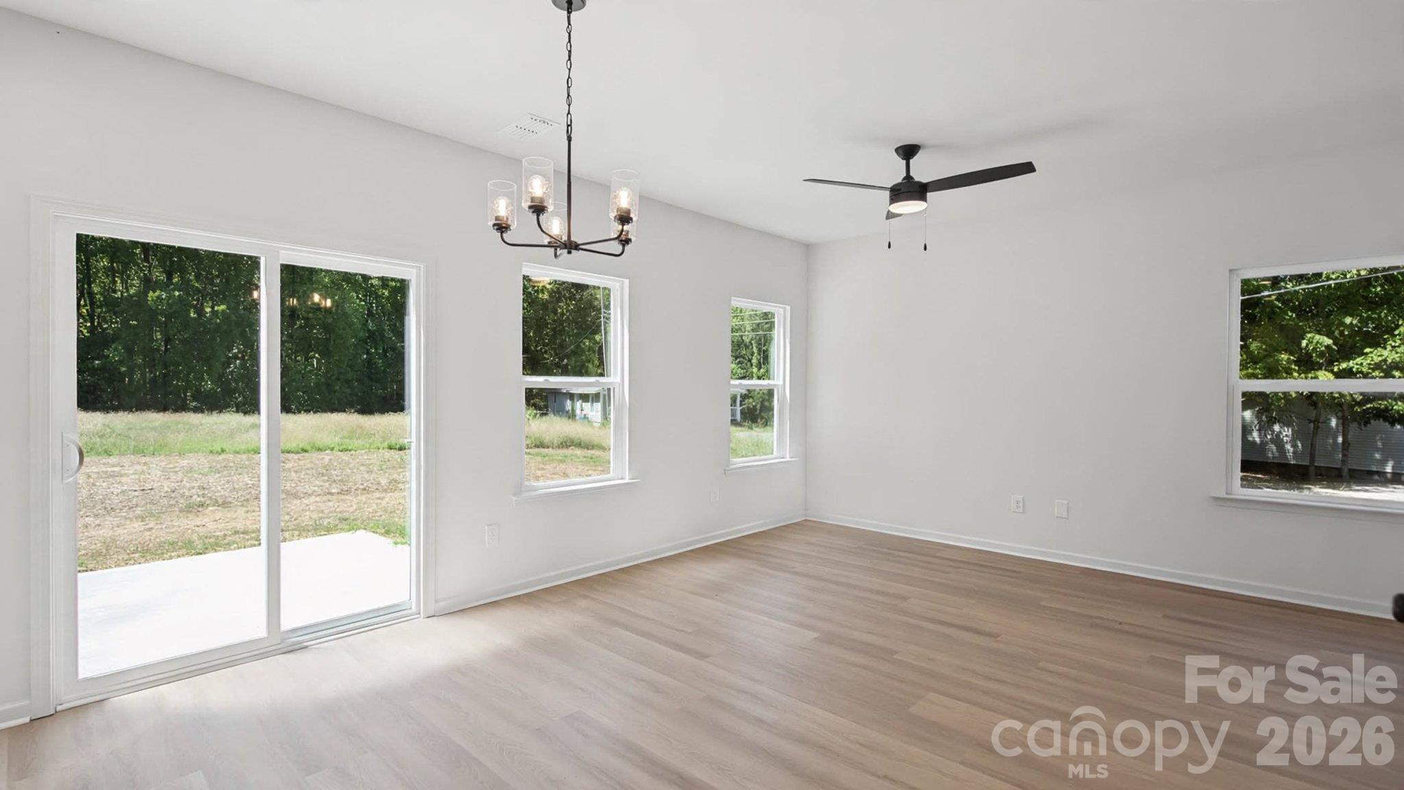 Vacant room with light wood floors, a sliding glass door, multiple windows, and a ceiling fan.