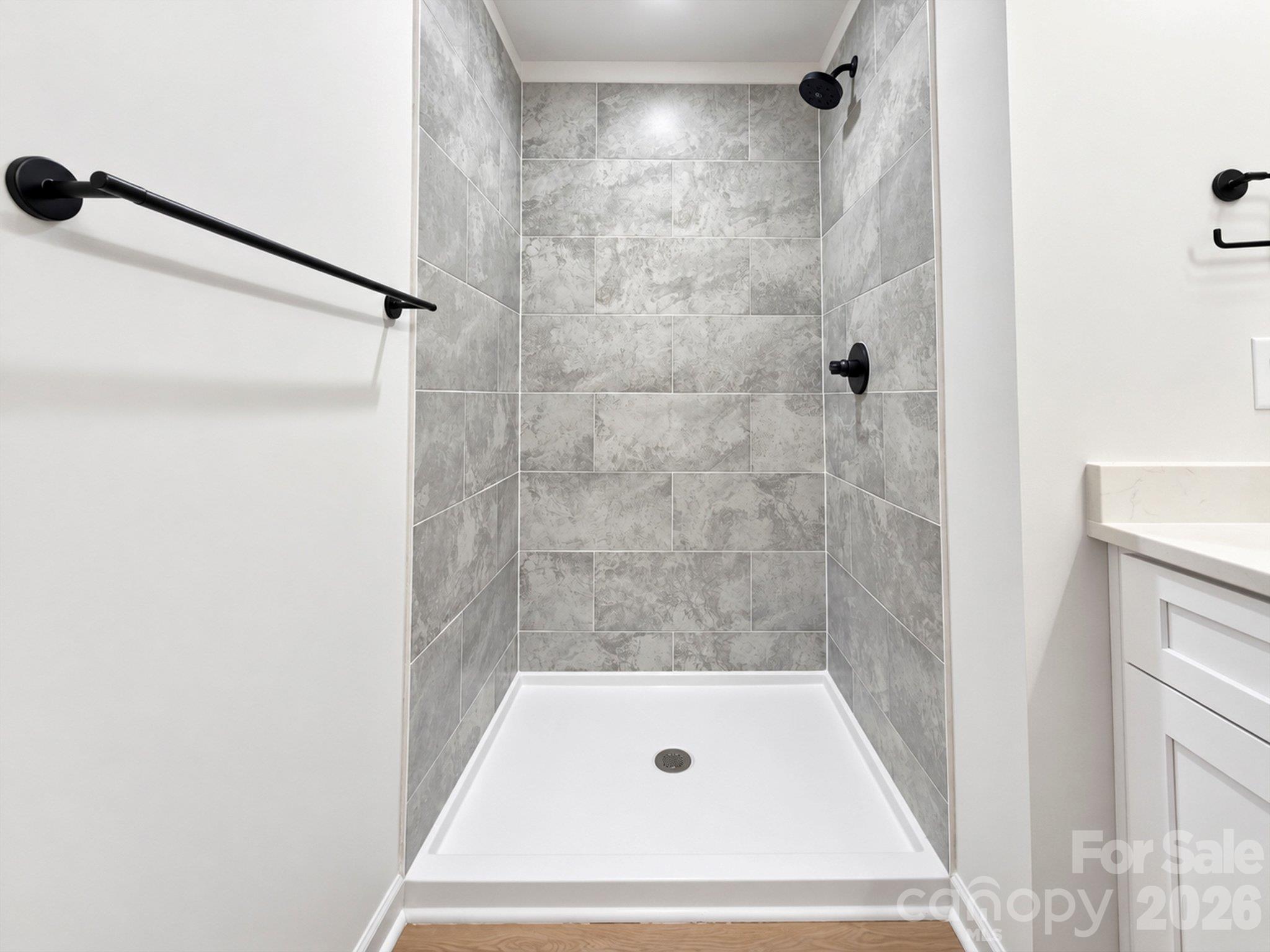 Gray-tiled walk-in shower with matte black fixtures and a white shower pan.