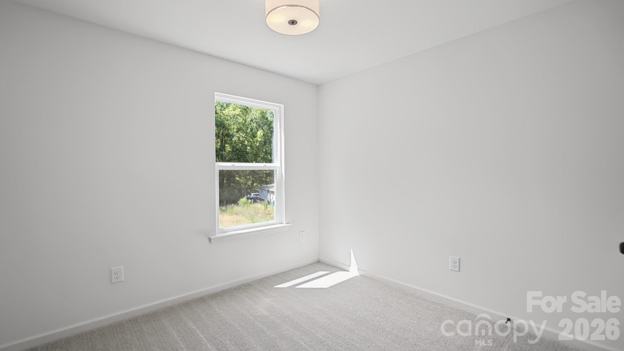 Empty bedroom with light carpet, white walls, and a window overlooking trees.
