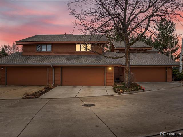Two-story brown home with three garage doors and a leafless tree at dusk.