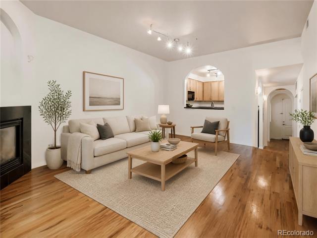Staged living room with a cream sofa, hardwood floors, and an arched opening to the kitchen.