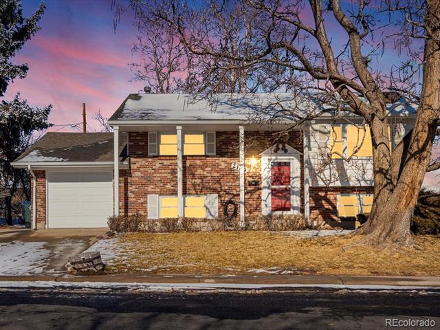 Two-story brick house with an attached garage and a large leafless tree in the front yard.