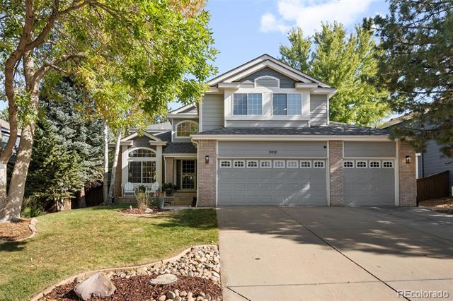 Two-story home with a three-car garage, brick accents, and mature trees framing the front yard.