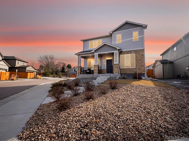 Two-story gray home with stone accents and a rock-covered front yard at dusk.