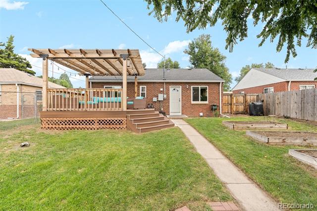Brick home with a raised wooden deck and pergola overlooking a fenced backyard.