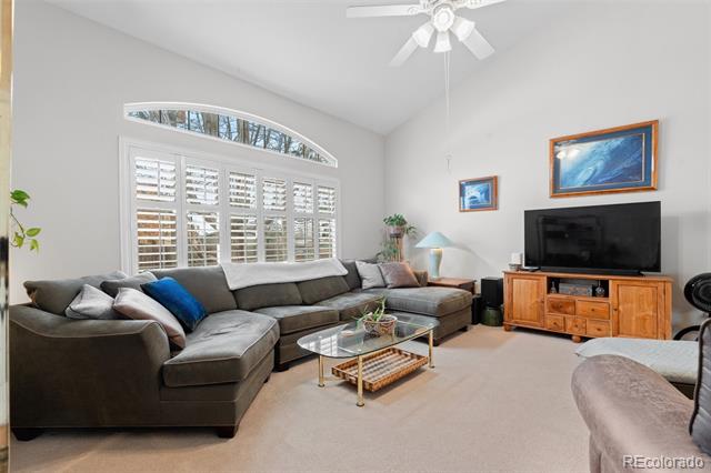 Living room with a gray sectional, arched shuttered window, glass coffee table, and wooden TV console.