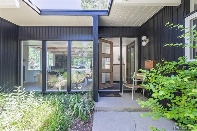 Modern home entrance with dark vertical siding, glass doors, and a landscaped walkway.