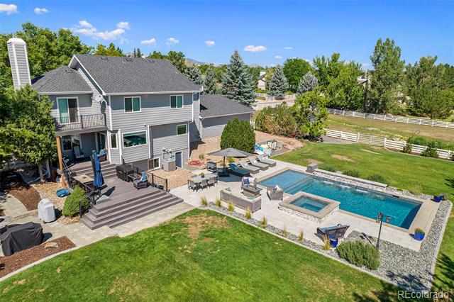Aerial view of a gray two-story home with a swimming pool, spa, and furnished backyard patio.