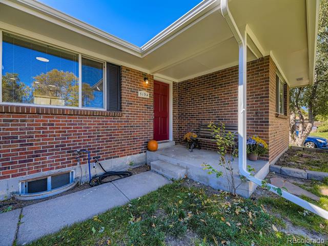 Brick home entrance with a red front door, covered porch, and concrete walkway.