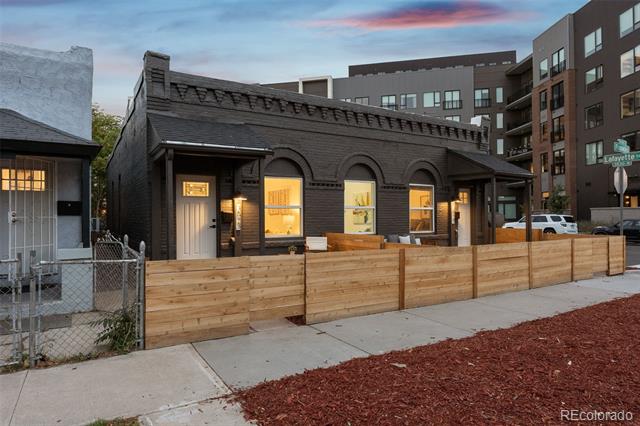 Dark single-story building with illuminated arched windows behind a wooden fence.