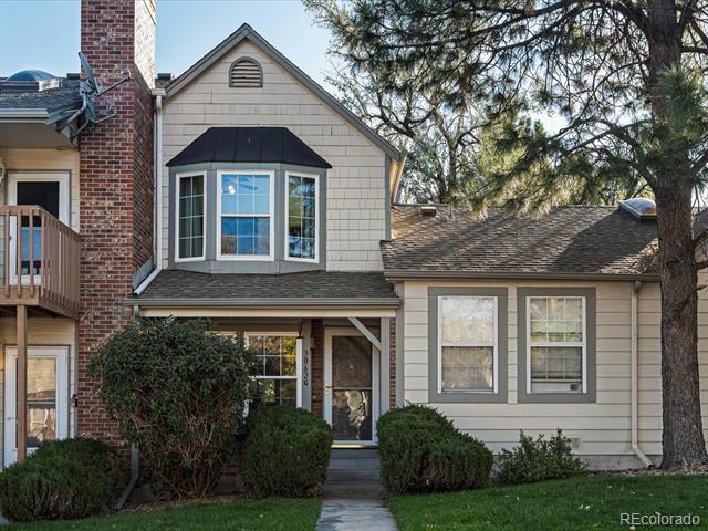 Two-story beige house with a brick chimney, upper bay window, and covered front entry.