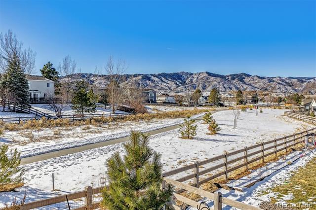 Snow-covered vacant lot with split-rail fencing and Rocky Mountain views.