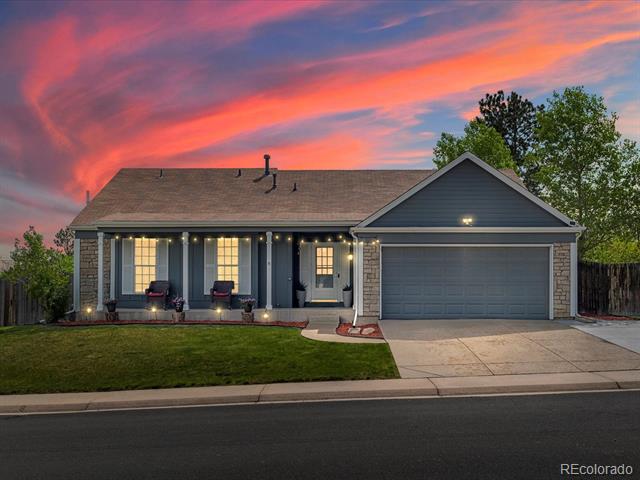 Gray single-story house with a stone-accented facade and attached garage under a vivid sunset.