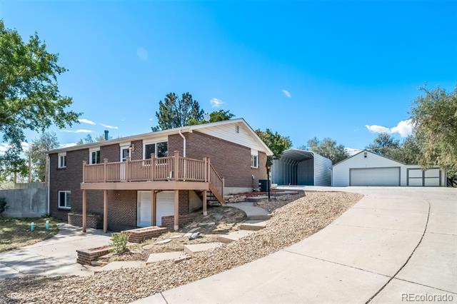 Two-story brick home with a raised deck beside a wide driveway and detached garage.